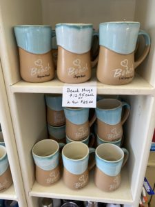 shelf holding ceramic beach mugs with names of local beaches etched into them